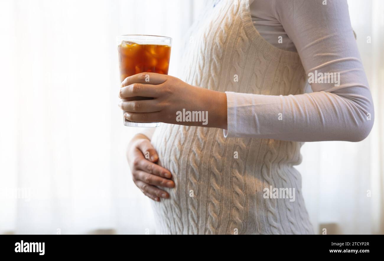 A pregnant woman is holding coffee by the window Stock Photo