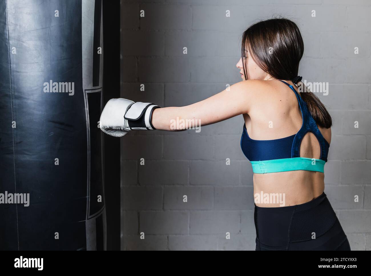 Horizontal photo pretty Caucasian teen girl Caucasian, brunette, dressed in sportswear and white boxing gloves, on white brick background. In the gym Stock Photo