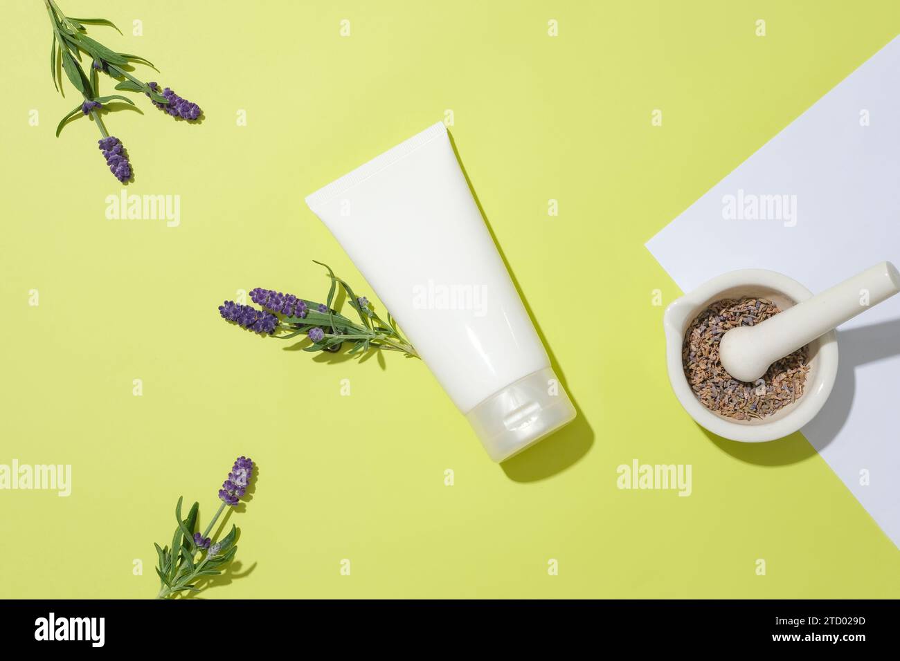 An unlabeled cosmetic tube is in the center of the frame, surrounded by decorations of lavender flowers and dried lavender buds inside a ceramic morta Stock Photo