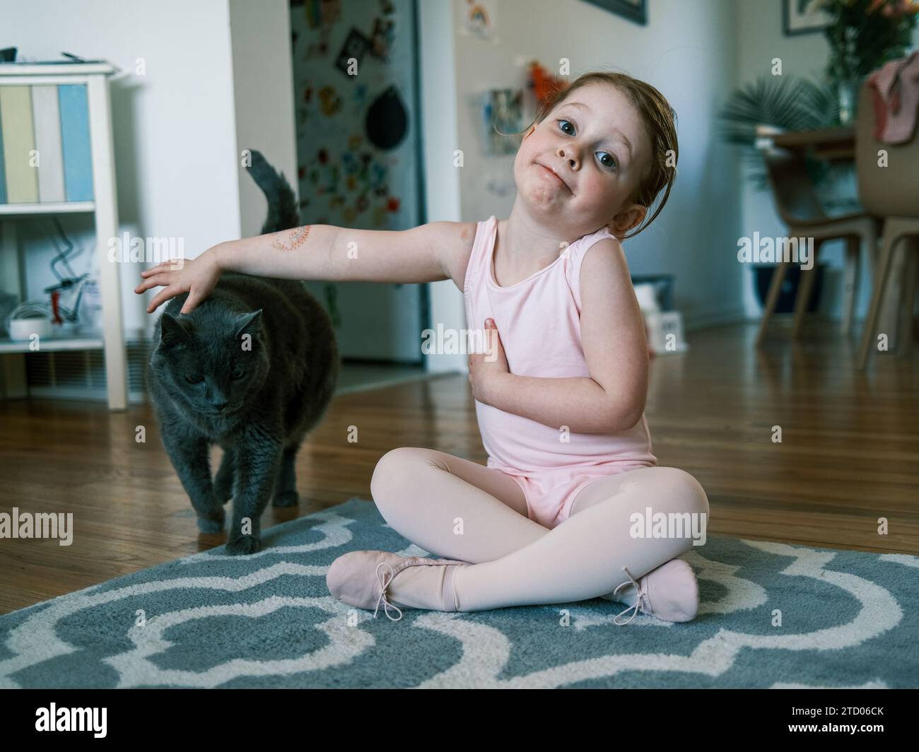 Happy toddler in ballet outfit petting a cat Stock Photo