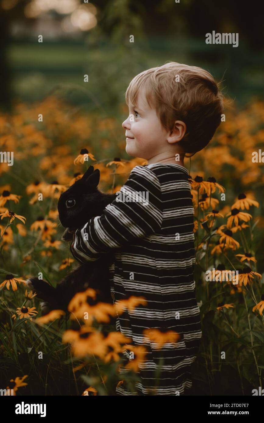 boy holding black fluffy bunny in flowers Stock Photo