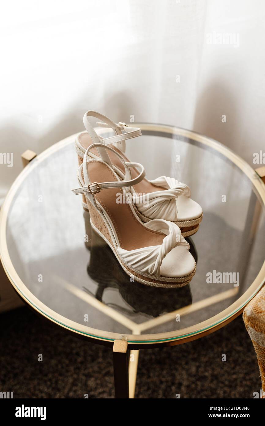 Bride's white wedding highheel shoes on glass table Stock Photo