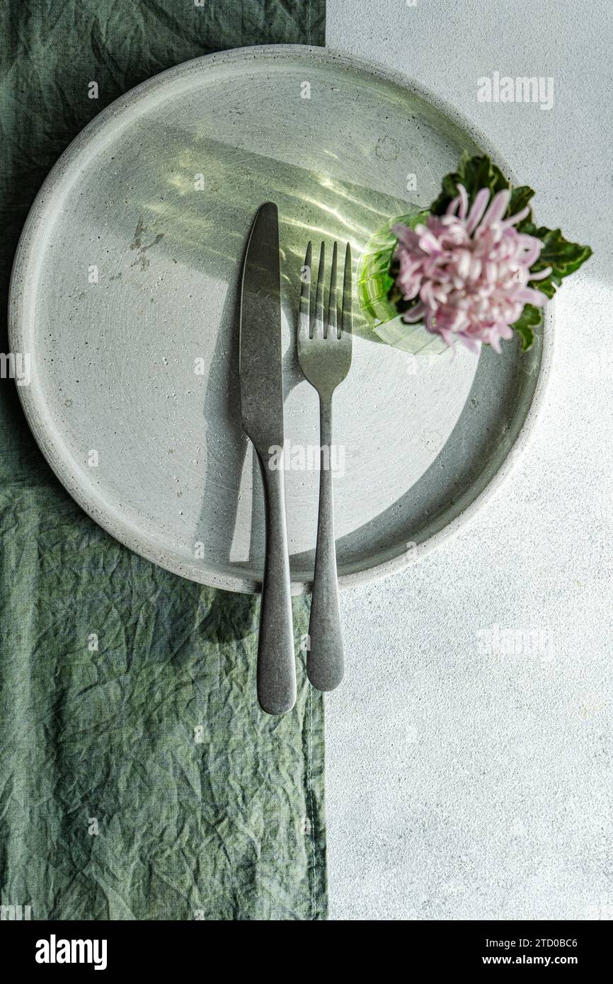 A top-down view of a chic table setting featuring a plate, cutlery, and a fresh flower on a textured cloth. Stock Photo