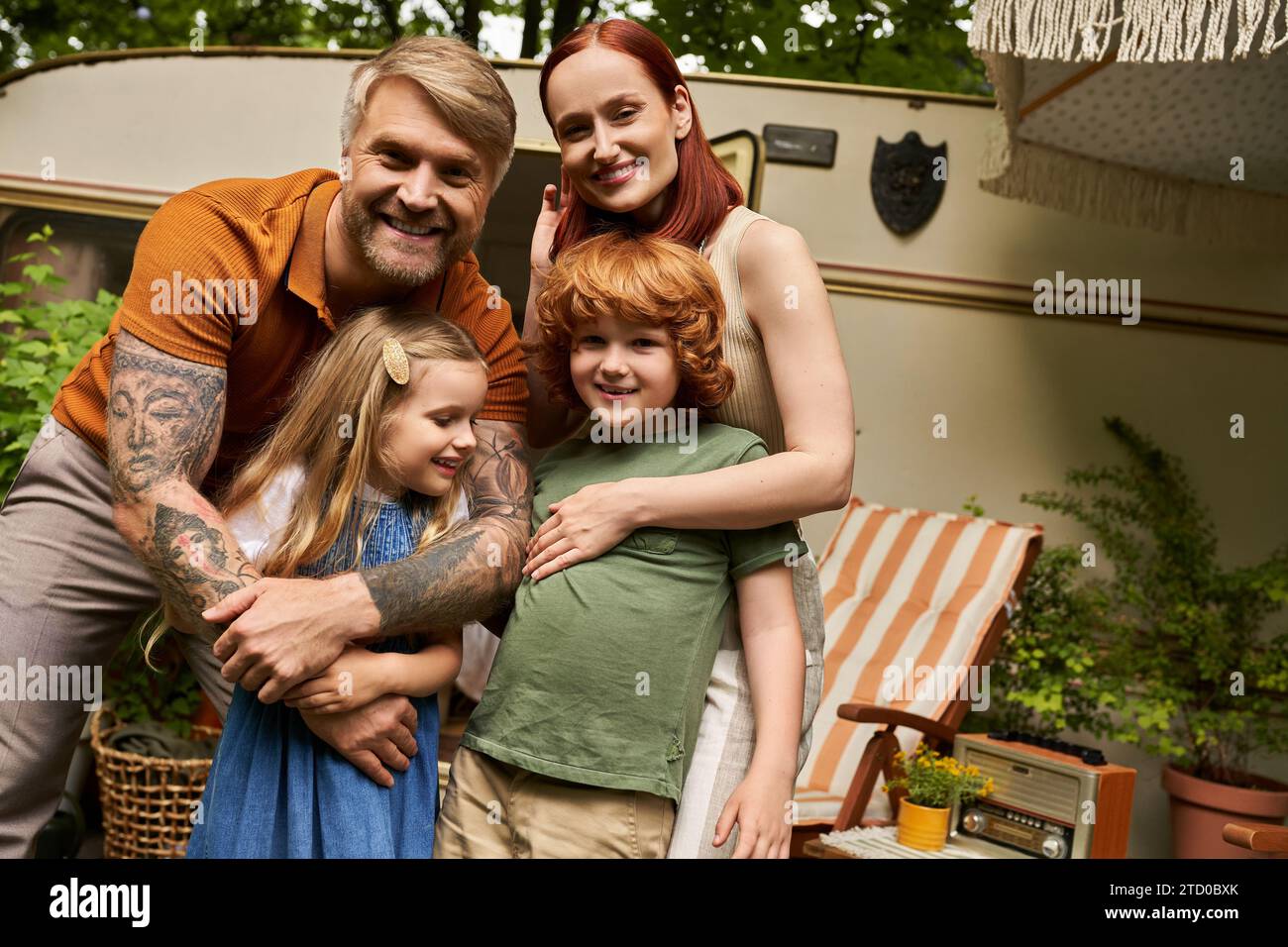 cheerful parents embracing happy kids near modern home on wheels in trailer park, family leisure Stock Photo