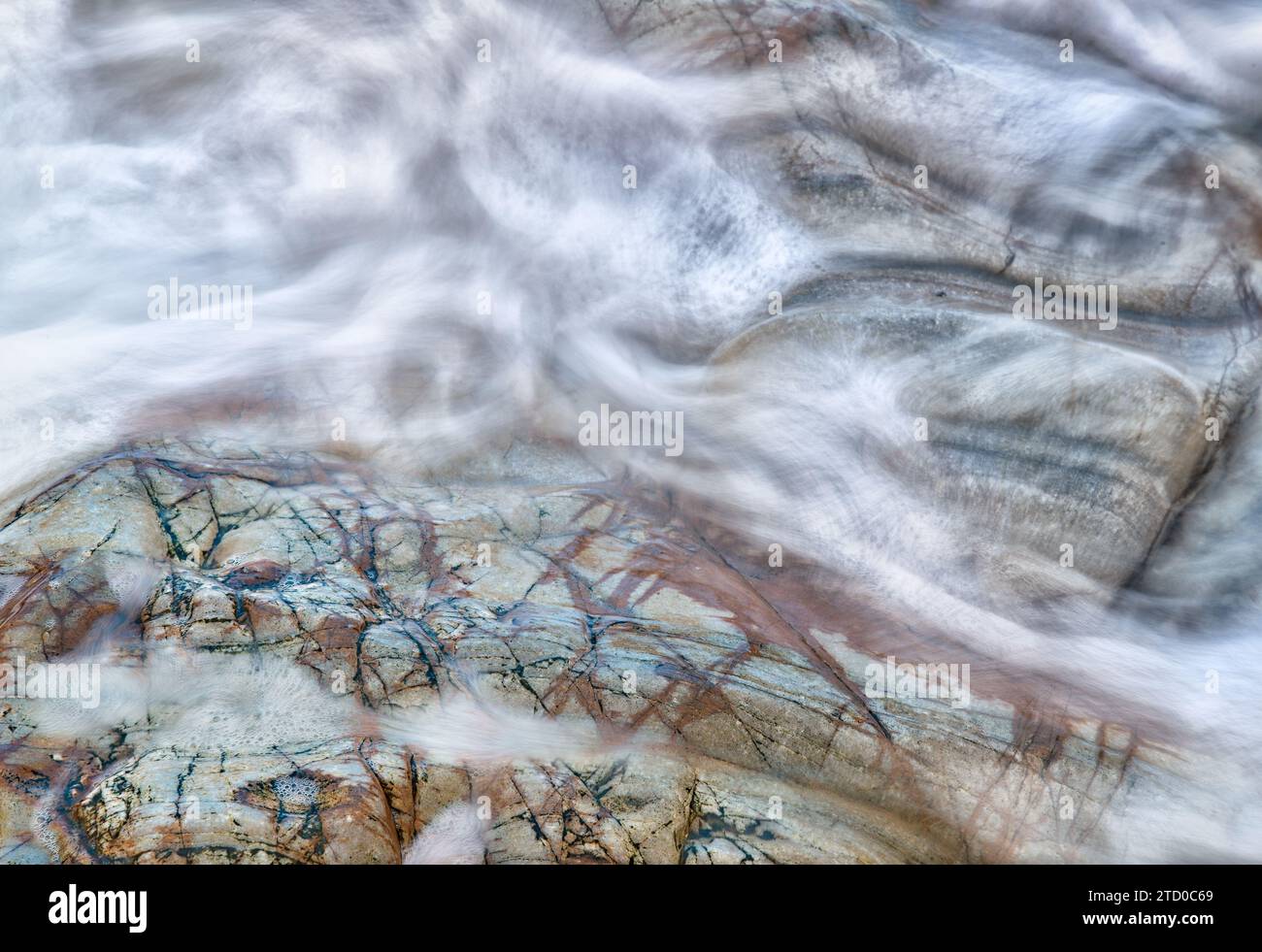 Smooth water flows create a ghostly veil over the multi-colored stone surface beneath. Stock Photo
