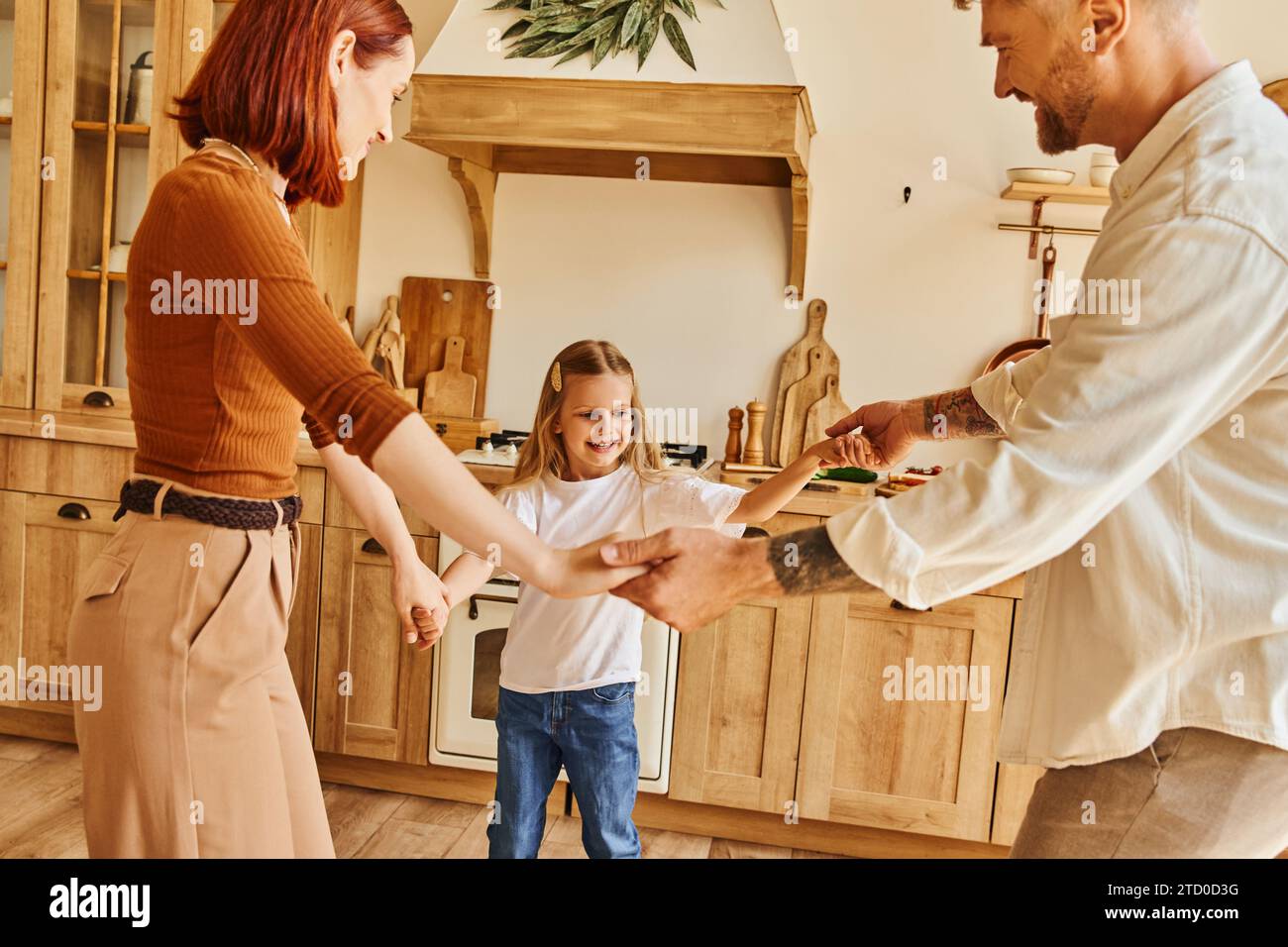 cheerful parents with adorable daughter holding hands and playing in kitchen, fun and laughter Stock Photo