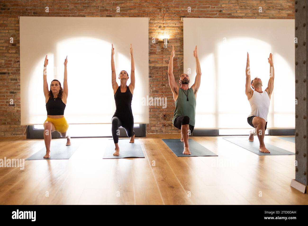 A group of three adults engage in a yoga session inside a bright ...
