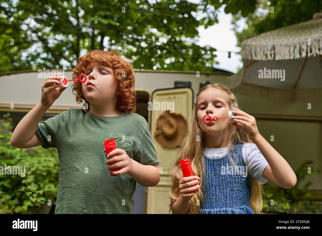 Redhead Brother And Blonde Sister Blowing Soap Bubbles Near Trailer