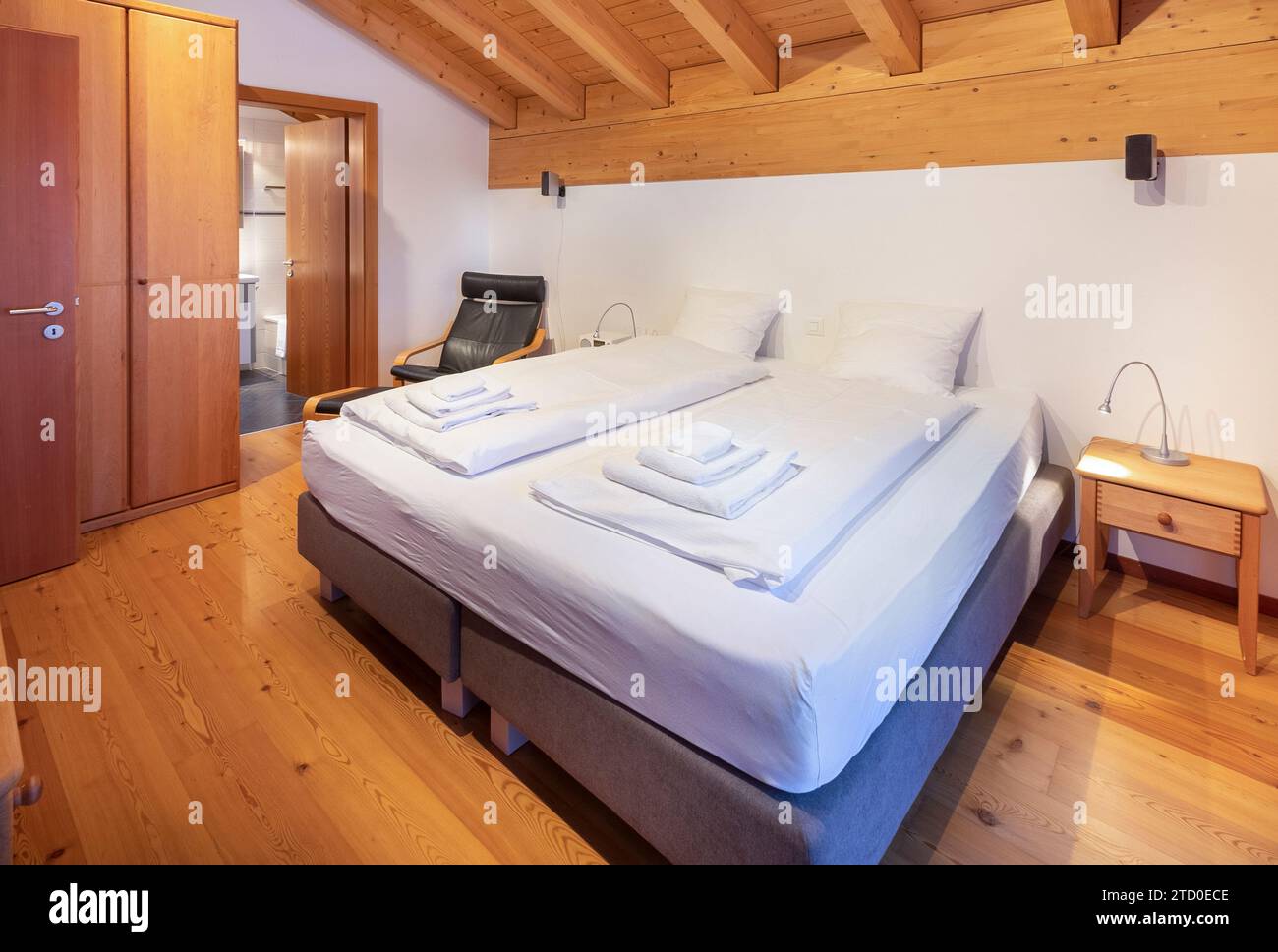 A warm and inviting wooden chalet bedroom interior with neat bedding and traditional furnishings, reflecting the rustic charm of Zermatt accommodation Stock Photo