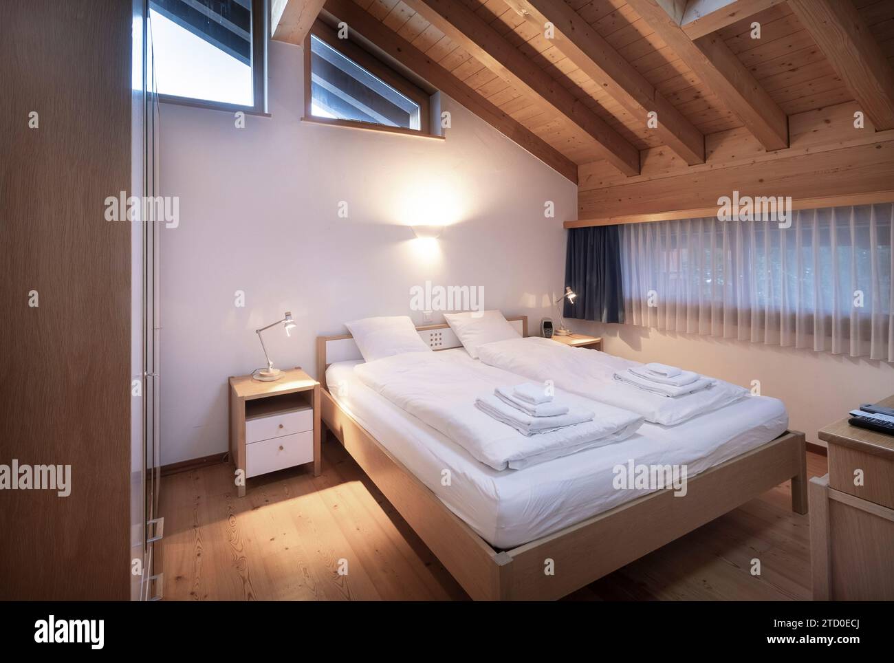 Modern and welcoming chalet bedroom interior featuring wooden beams, a comfortable double bed, and a warm lighting ambiance. Stock Photo