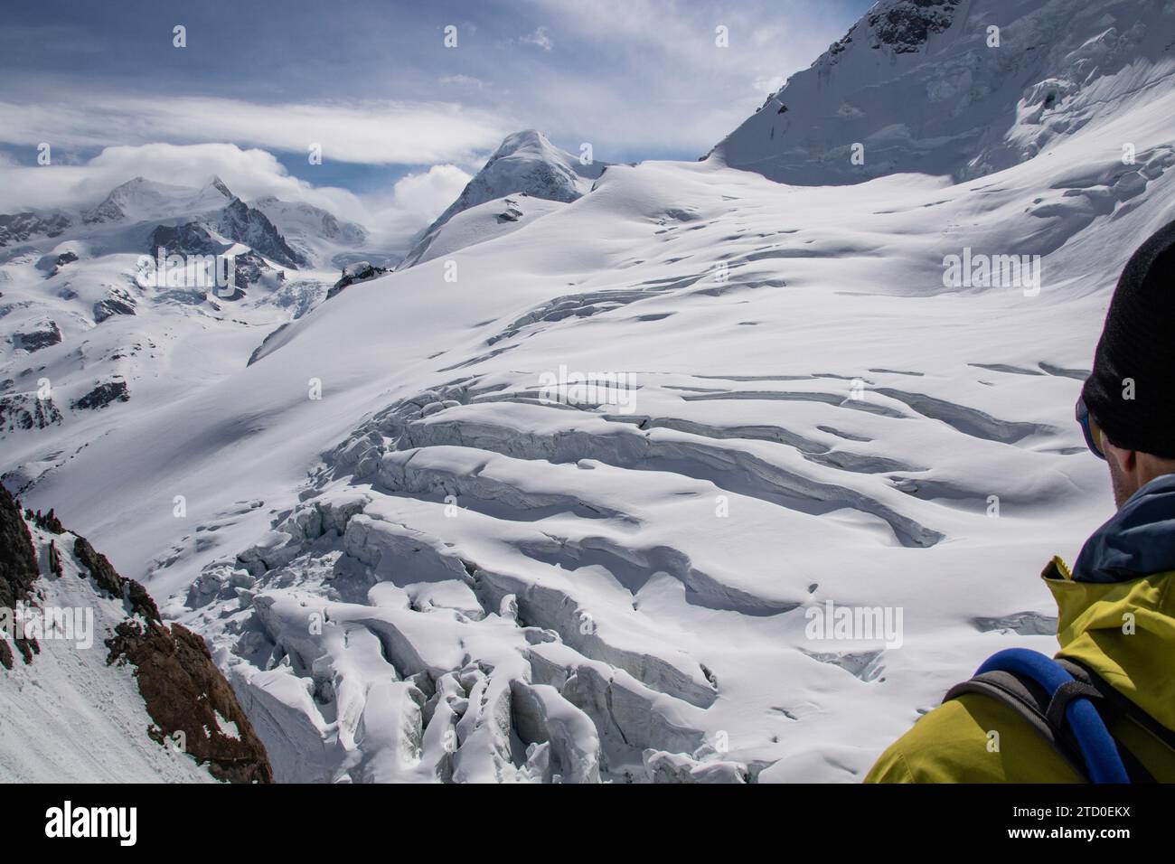 High angle of crop anonymous man in warm clothes and knit cap standing near snow-covered rocky mountain during hiking in Zermatt, Switzerland Stock Photo