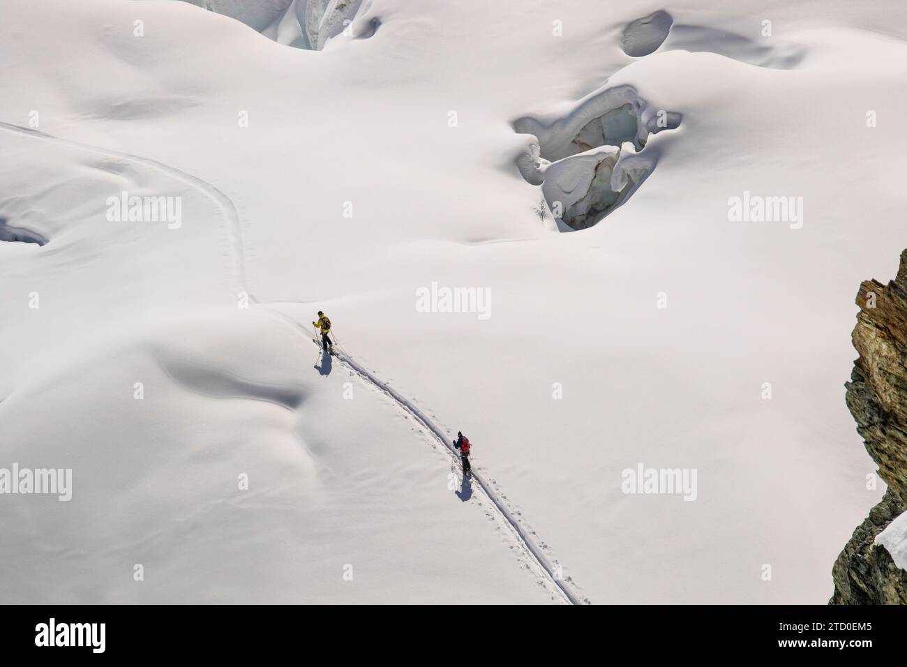 High angle of anonymous skiers in warm clothes making their way across the pristine, snow