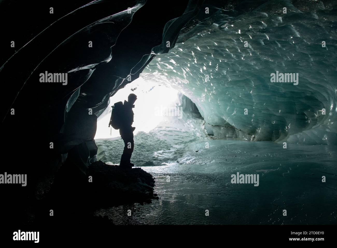Side view of unrecognizable silhouette traveler with backpack standing on ice surface and exploring cave during winter vacation in Canada Stock Photo