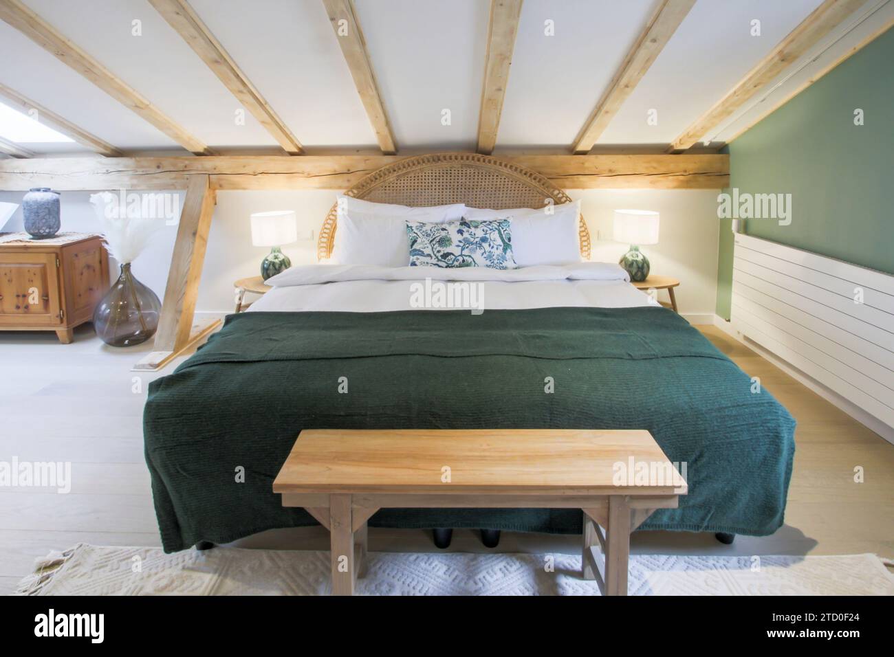 An inviting attic bedroom featuring exposed wooden beams, a plush green ...