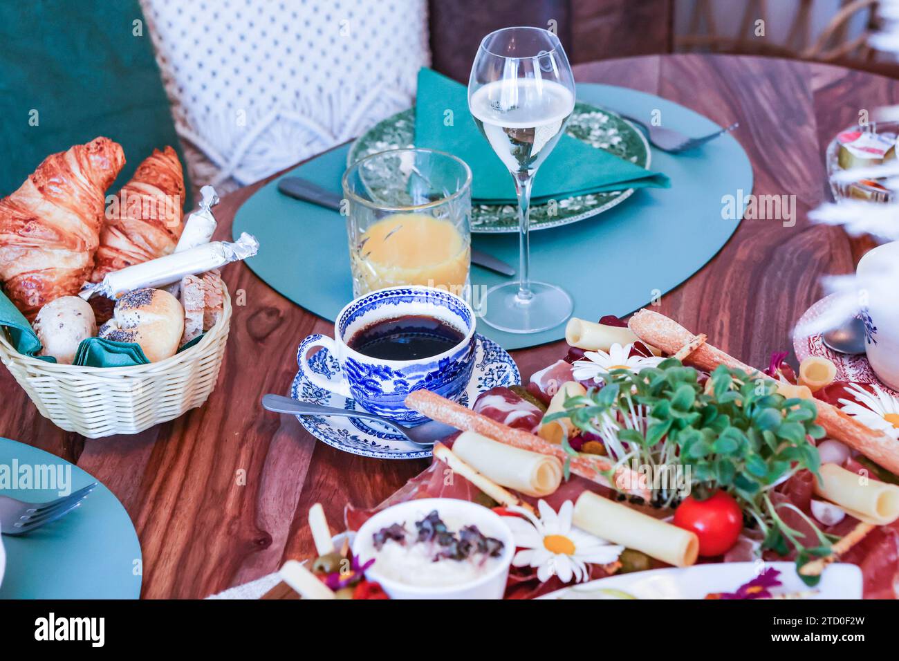 A well-appointed brunch table featuring a variety of foods including fresh croissants, cold cuts, and cheese, accompanied by coffee, juice, and wine. Stock Photo