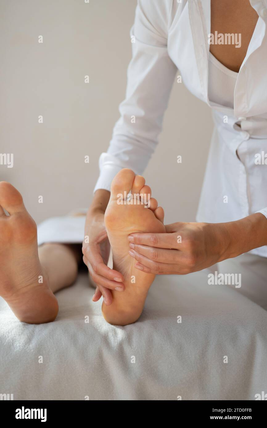 Crop hands of anonymous female therapist massaging foot of customer lying on bed to relieve pain by gently pressing pressure points at spa salon Stock Photo