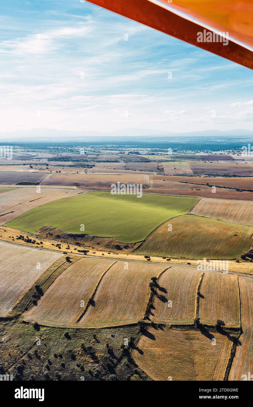 The vibrant patchwork of agricultural fields unfolds below from an aerial perspective, seen from the vantage point of a small aircraft's wing Stock Photo