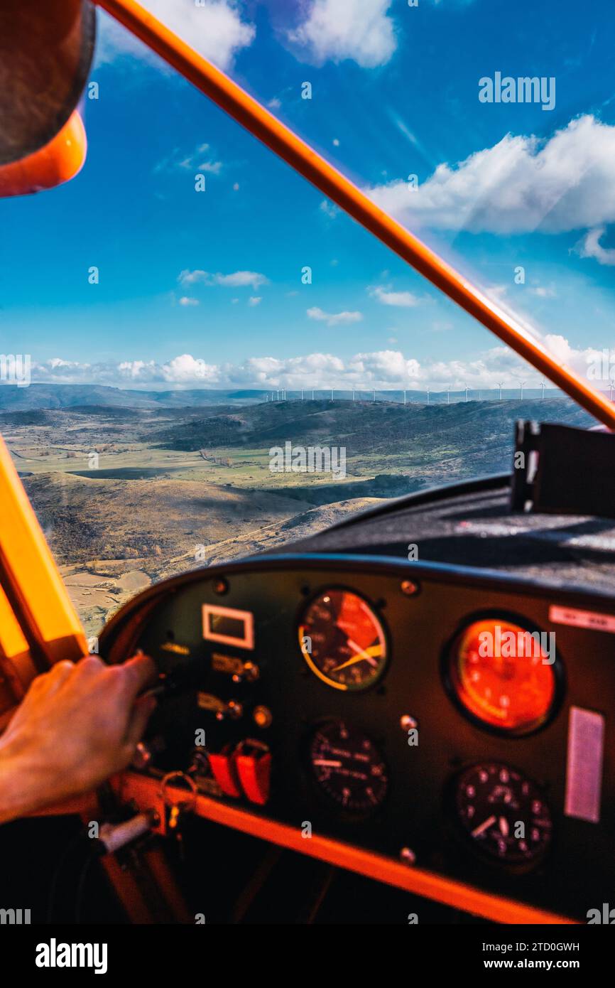 A pilot's hand is seen on the controls of a small aircraft, flying above a breathtaking landscape on a cloudy day Stock Photo