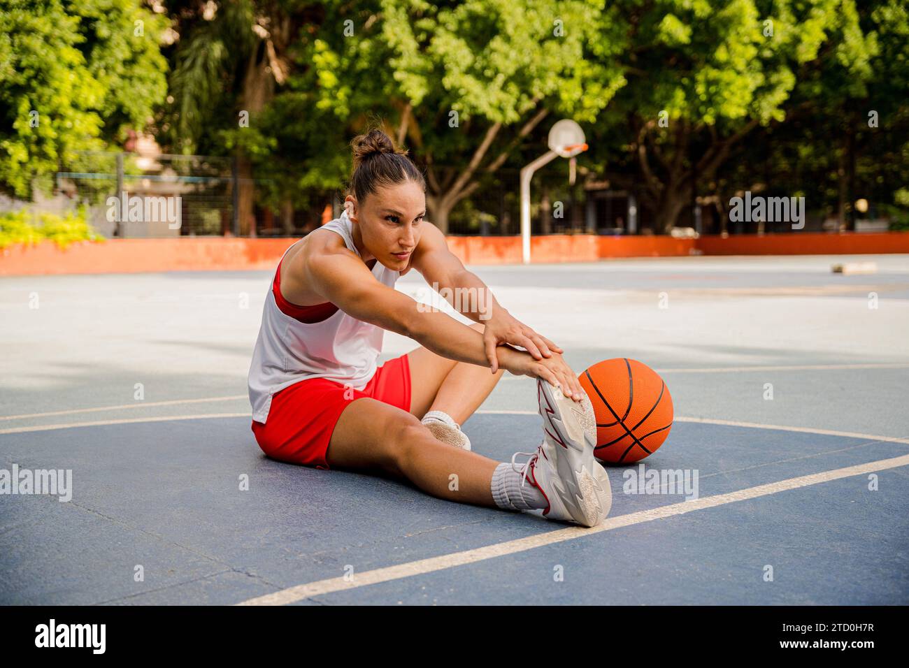Full body of determined young female basketball player sitting and