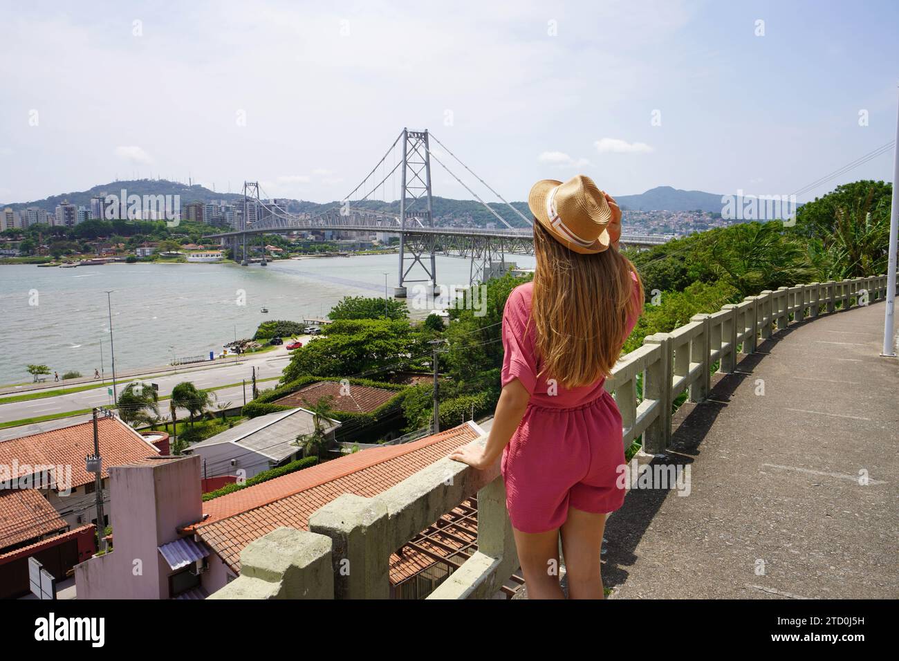 Holidays in Florianopolis, Brazil. Rear view of beautiful stylish traveler girl enjoying view of Hercilio Luz bridge in Florianopolis, Brazil. Summer Stock Photo
