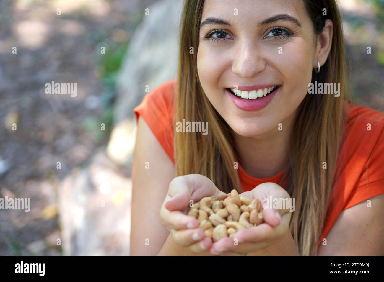 Beautiful healthy girl showing cashew nuts in her hands outdoors. Looks st camera. Stock Photo