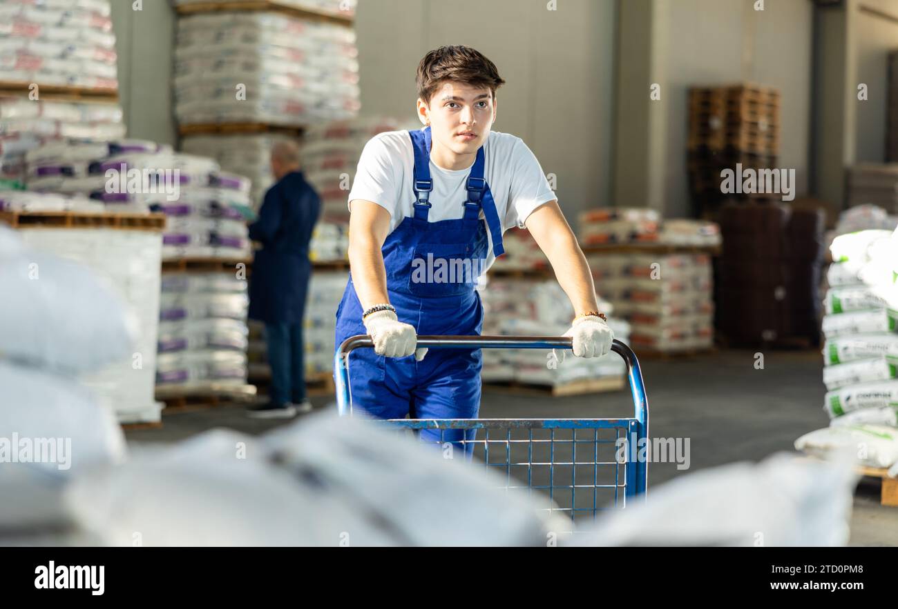 Young loader guy pushing cart in warehouse Stock Photo