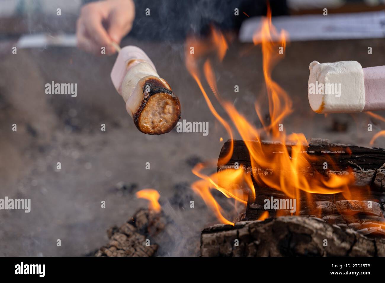 Southampton, England - December 8, 2023: Hands holding marshmallows on a wooden skewer over a fire. Grilled marshmallows *** Hände halten Marshmallows auf einem Holzspieß über ein Feuer. Gegrillte Marshmallows Stock Photo