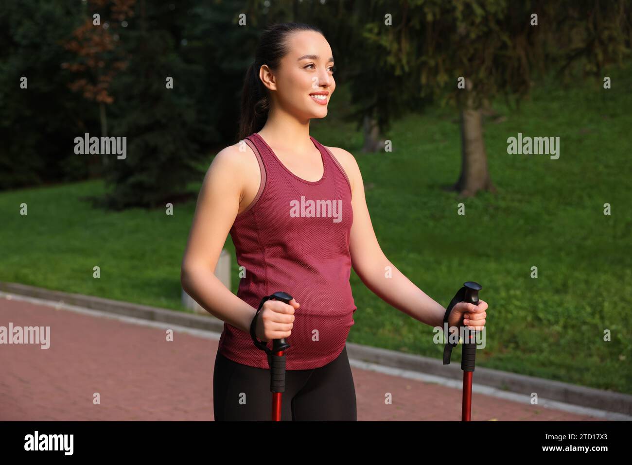 Pregnant woman practicing Nordic walking with poles outdoors Stock Photo