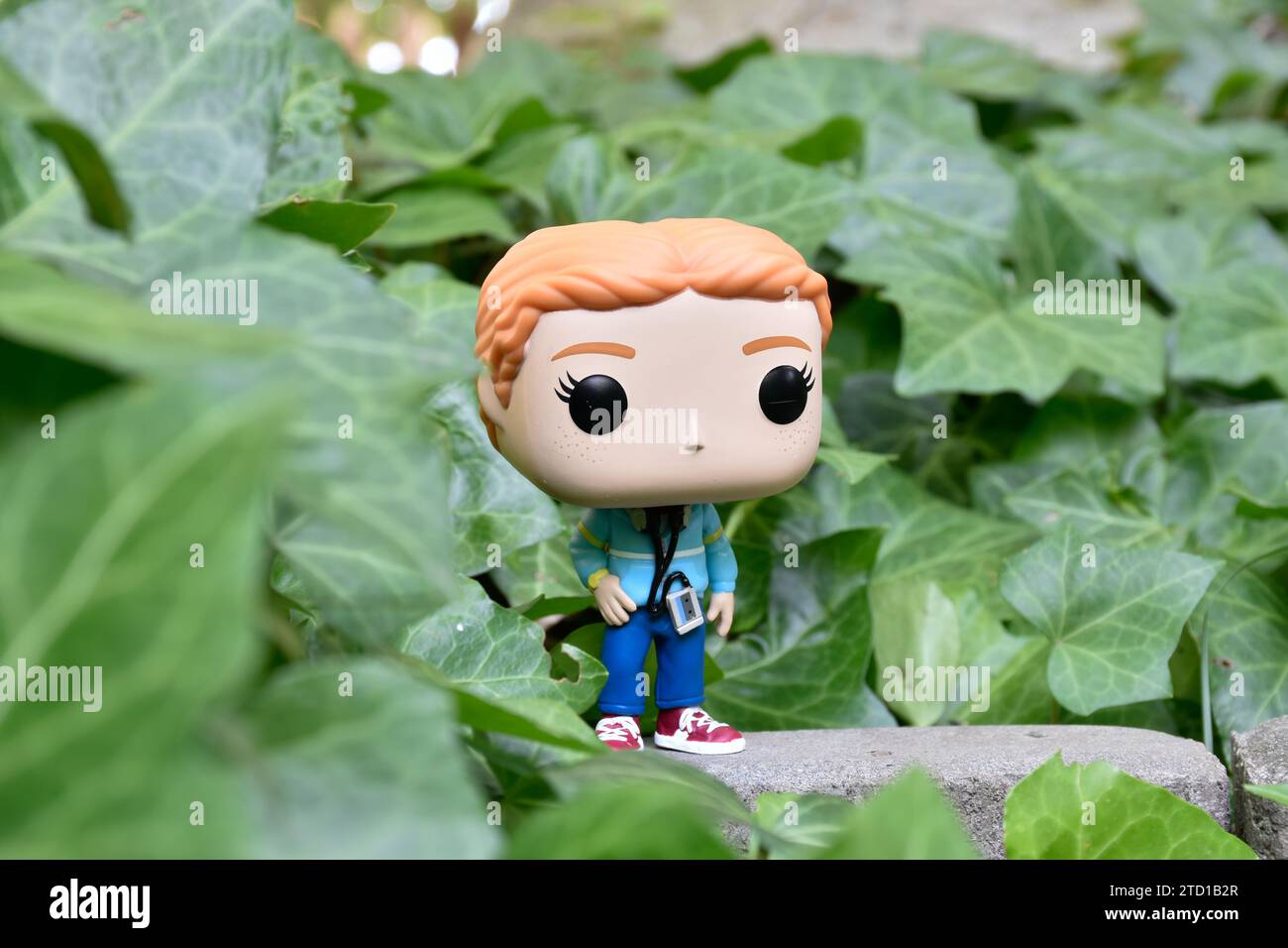 Funko Pop action figure of Max Mayfield with cassette player from Netflix TV series Stranger Things. Green ivy plant leaves, abandoned garden. Stock Photo