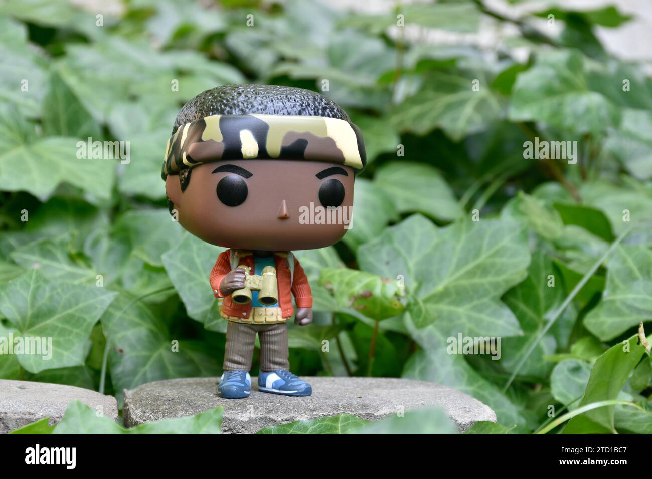 Funko Pop action figure of Lucas Sinclair with binoculars from Netflix TV series Stranger Things. Green ivy plant leaves, abandoned garden, spying. Stock Photo
