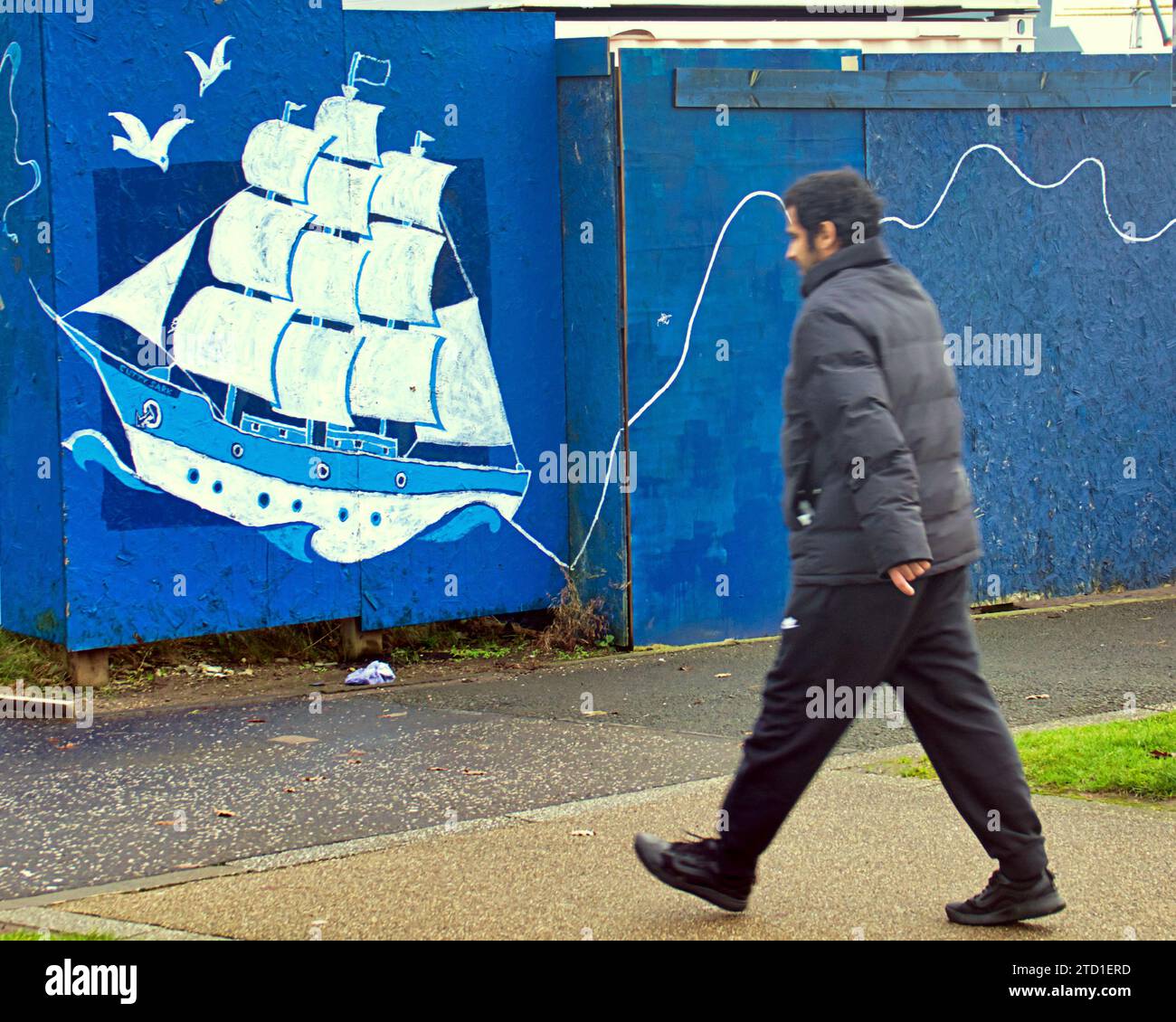 Glasgow, Scotland, UK. 15th December, 2023. UK Weather:  Cloudy  saw a miserable wet day  in the city Centre. As a walker passes the city's longest mural stretching for more than 500 metres, the piece celebrates the River Clyde a piece of community art named Dancing Wave. Credit Gerard Ferry/Alamy Live News Stock Photo