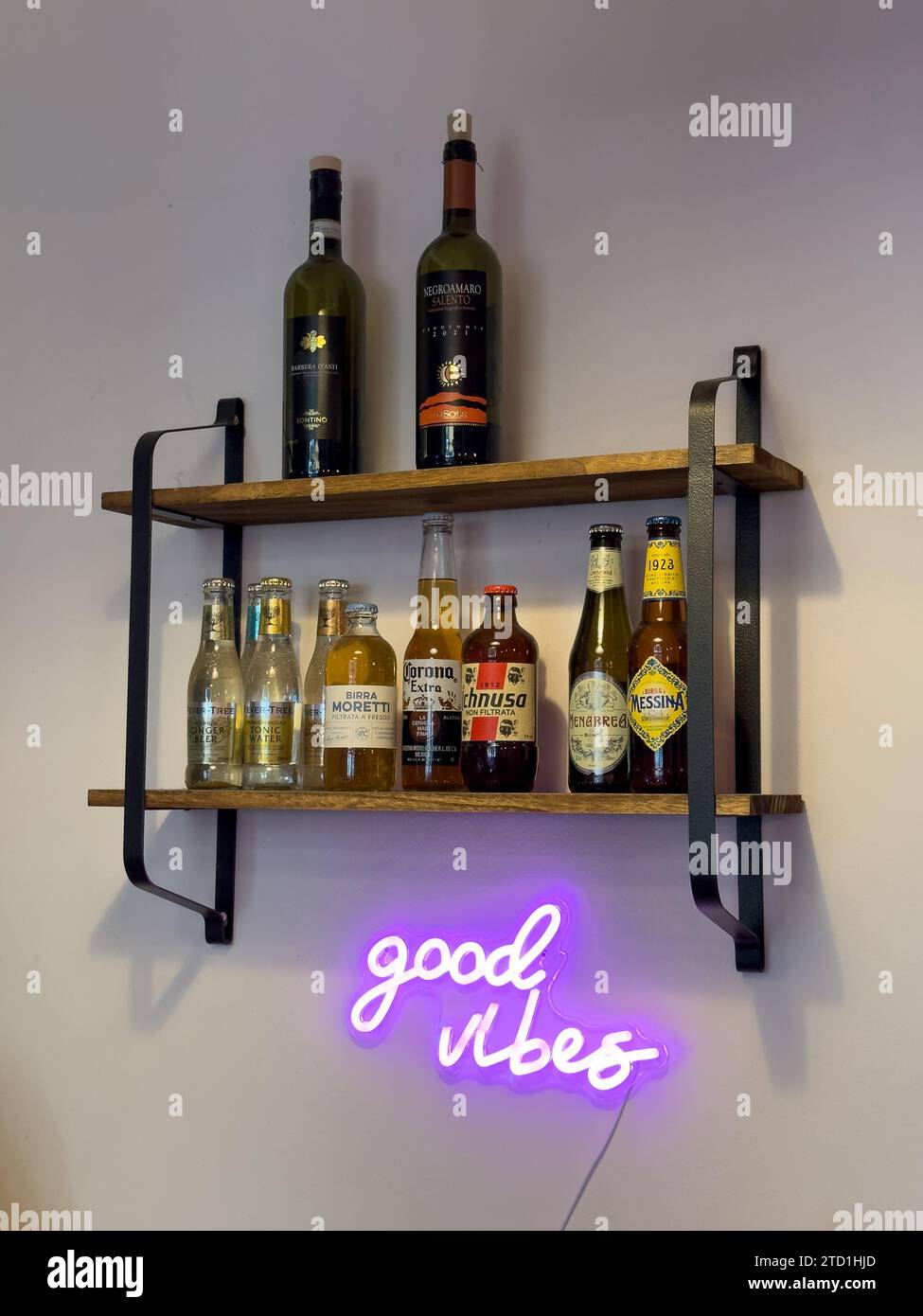 a beautiful bright pink neon 'good vibes' sign and shelf with selected beers on display, hanging on a white wall,in a nice trendy bar, in Milan, Italy Stock Photo