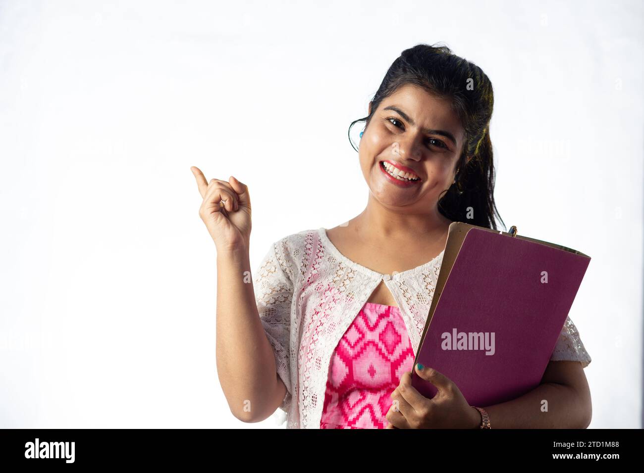A pretty young Indian girl with books in hand pointing with smiling ...