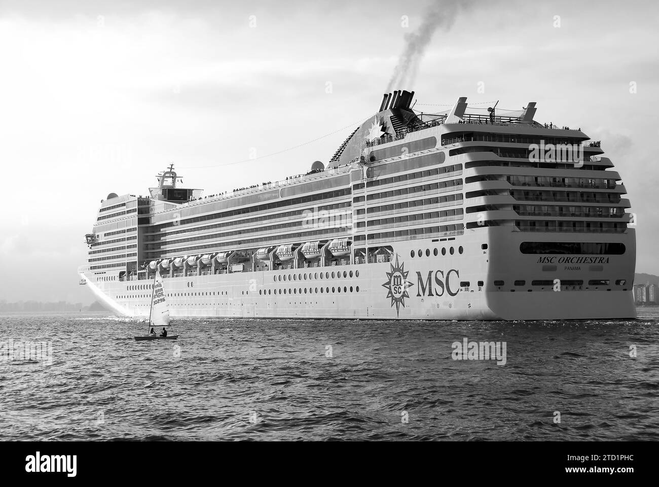 Cruise ship MSC Orchestra sailing during sunset. Sailboat next to the ship in the foreground. Black and white image. Santos city, Brazil. Stock Photo