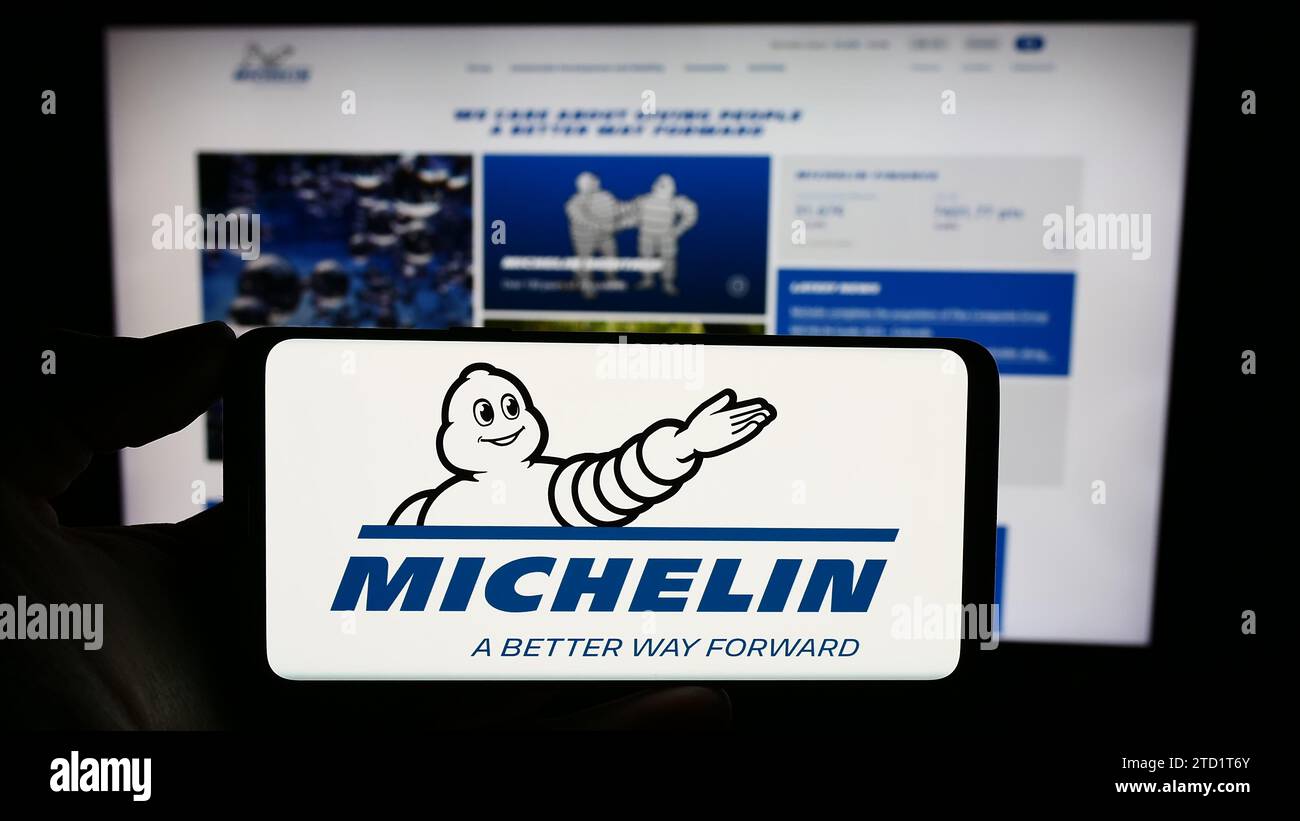 Person holding cellphone with logo of Compagnie Générale des Établissements Michelin SCA in front of business webpage. Focus on phone display. Stock Photo