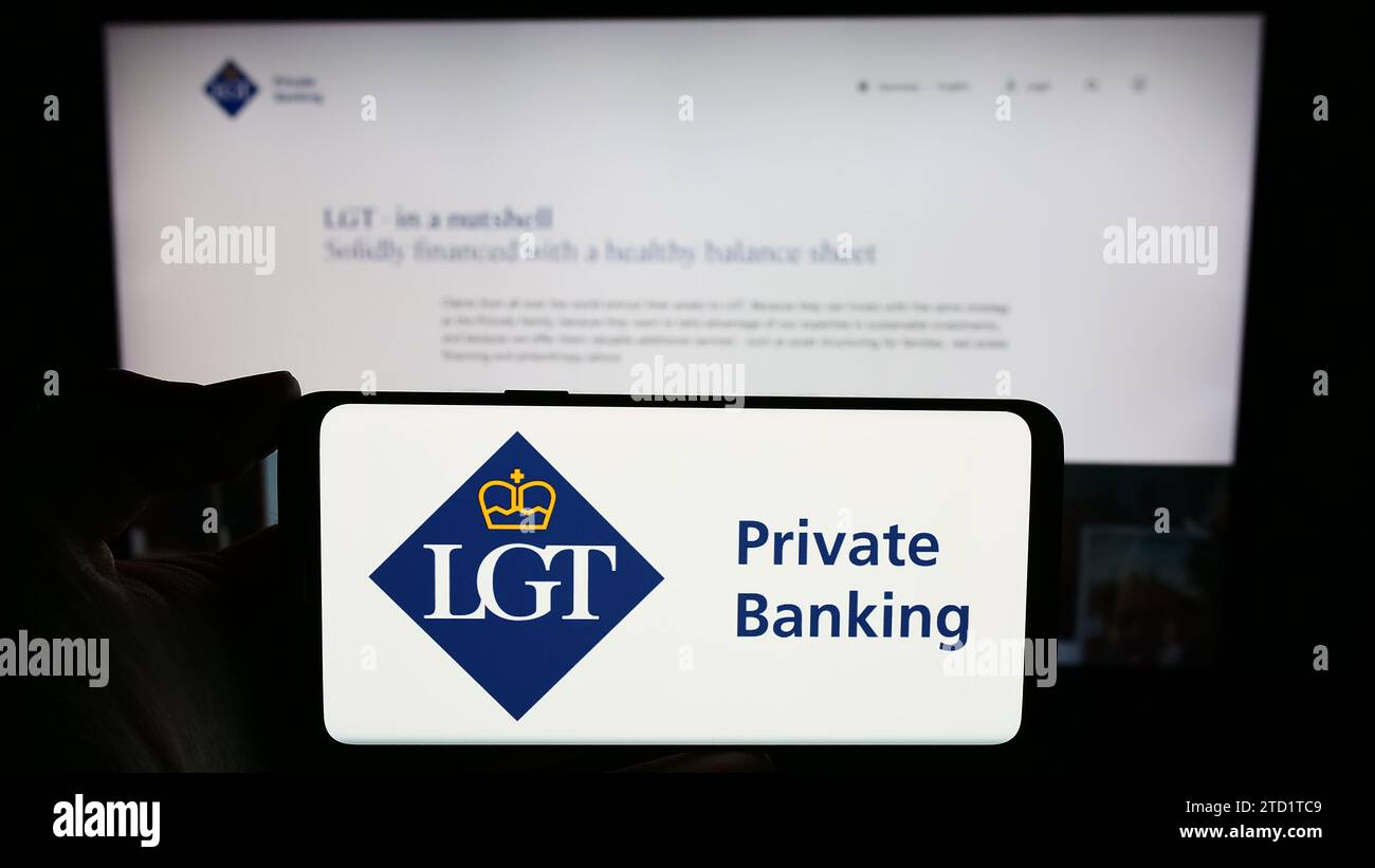 Person holding mobile phone with logo of Liechtenstein financial services company LGT Group in front of business web page. Focus on phone display. Stock Photo