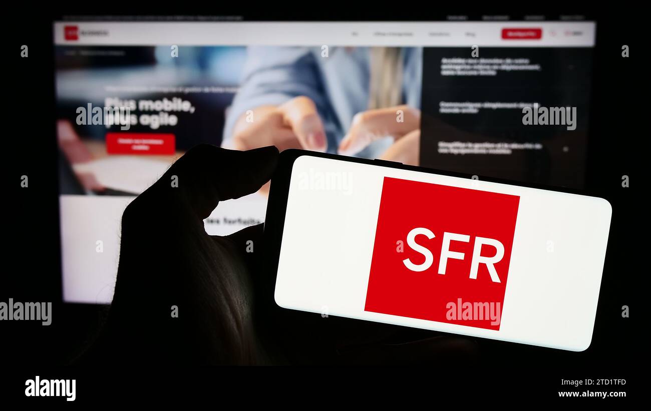 Person holding mobile phone with logo of French company Société Française du Radiotéléphone (SFR) in front of web page. Focus on phone display. Stock Photo