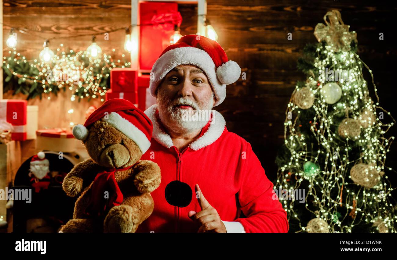 Christmas and New Year celebration. Santa Claus with teddy bear in room decorated for Christmas. Bearded man in Santa costume with teddy bear in Santa Stock Photo