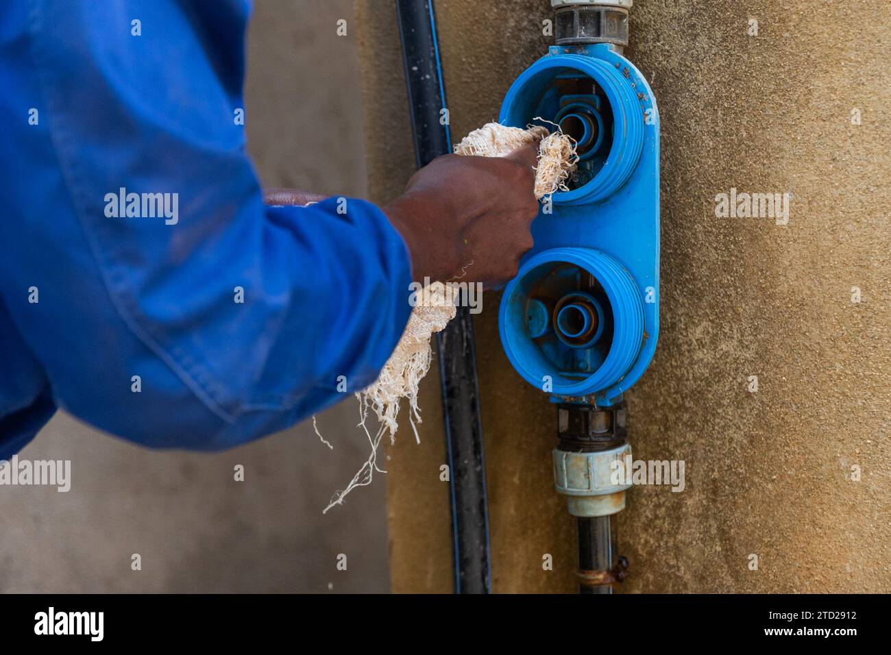 African plumber in blue overalls cleans water filter cartridge fittings. Stock Photo