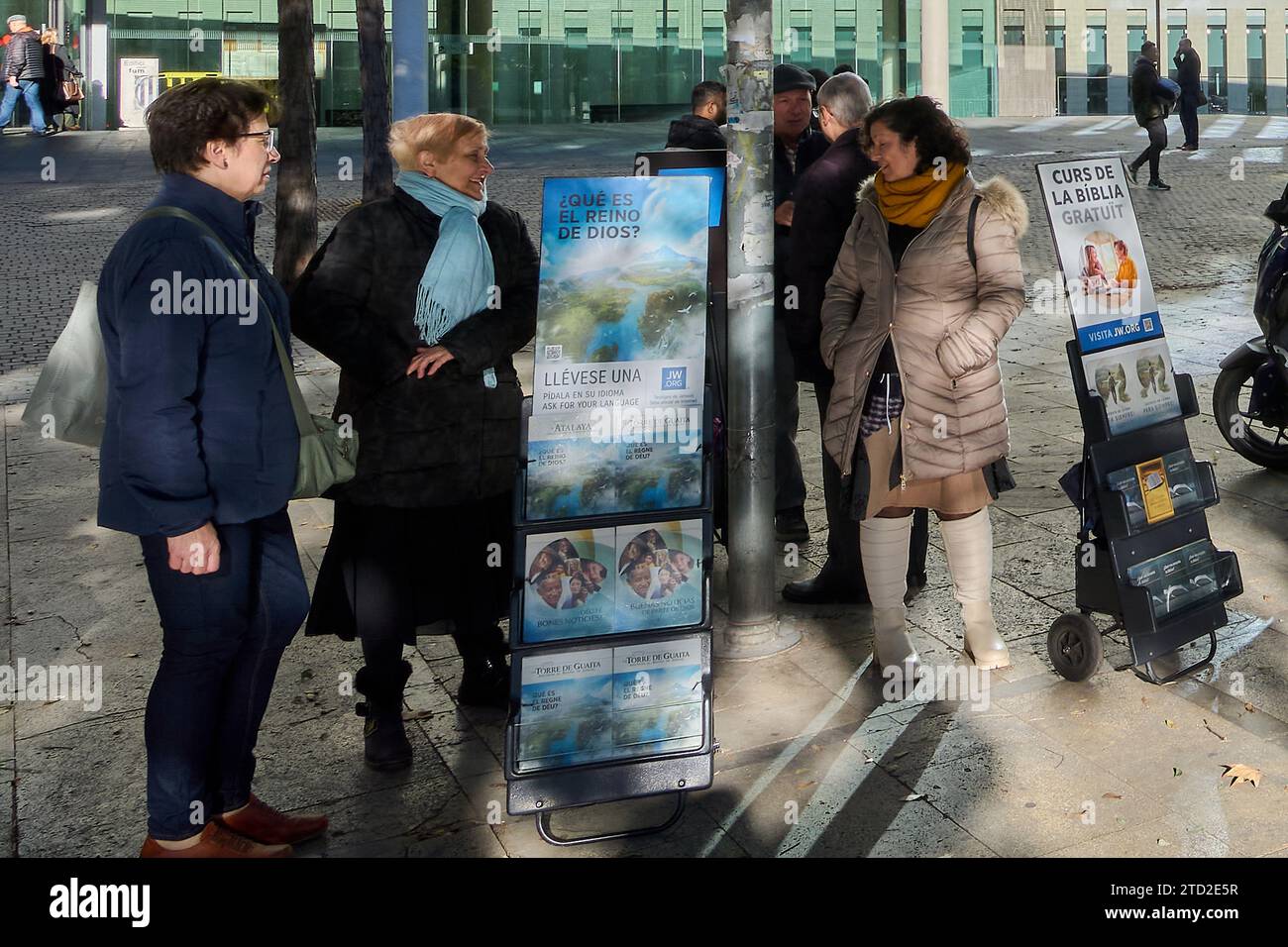 Barcelona - December 15, 2023: Group of people chatting on an urban street next to a religious advertisement in the City of Justice of Barcelona Spain Stock Photo