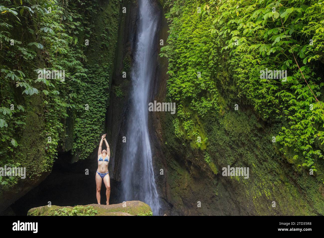 A young woman in a swimming suit at Leke Leke waterfall in lush ...