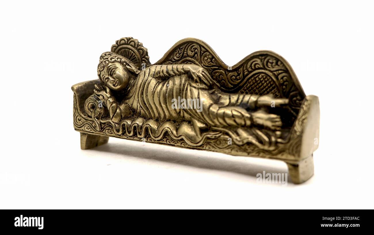 ancient figure handcrafted in gold colored metal of lord buddha sleeping on the side on a couch with pillow, with intricate details isolated Stock Photo