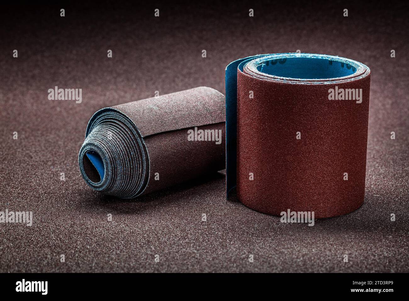 Big rolls of abrasive paper on background of biggest sheet of sandpaper