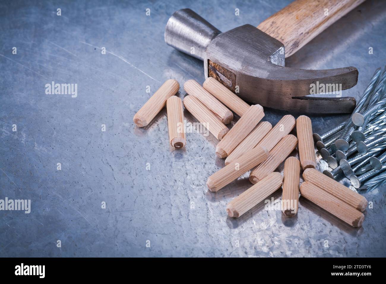 Claw hammer construction nails and wooden dowels on scratched metallic
