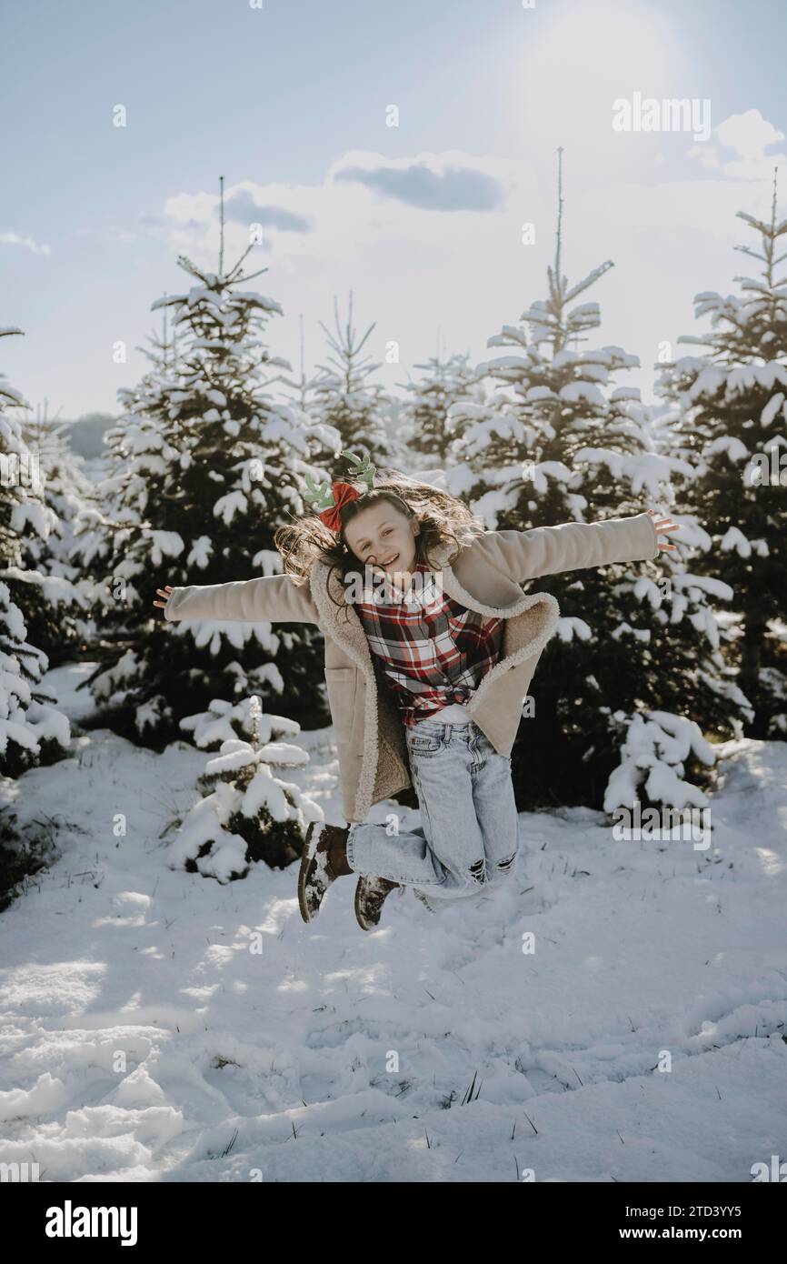 Girl in a winter coat in front of snow-covered fir trees Stock Photo