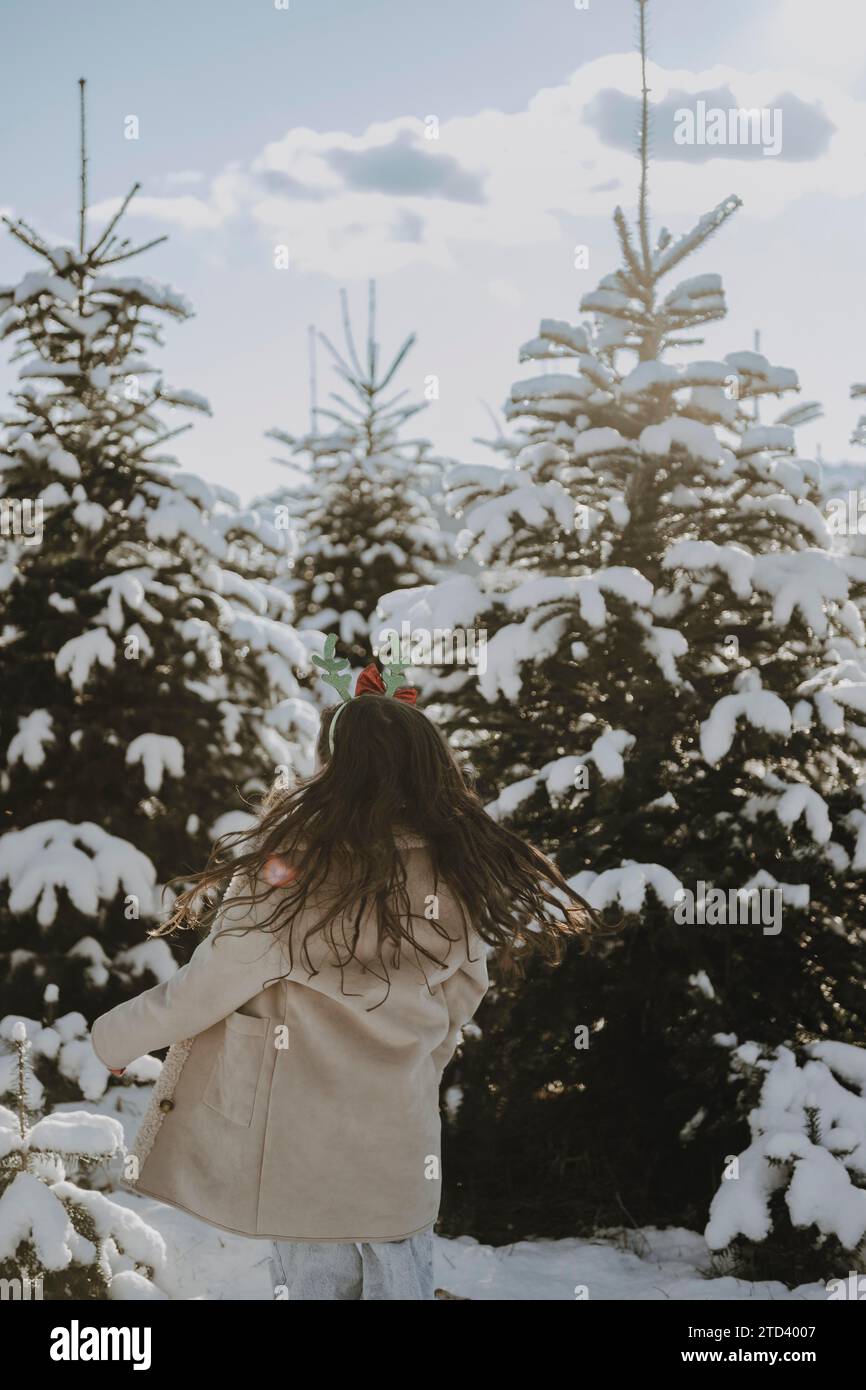 Girl in a winter coat in front of snow-covered fir trees Stock Photo