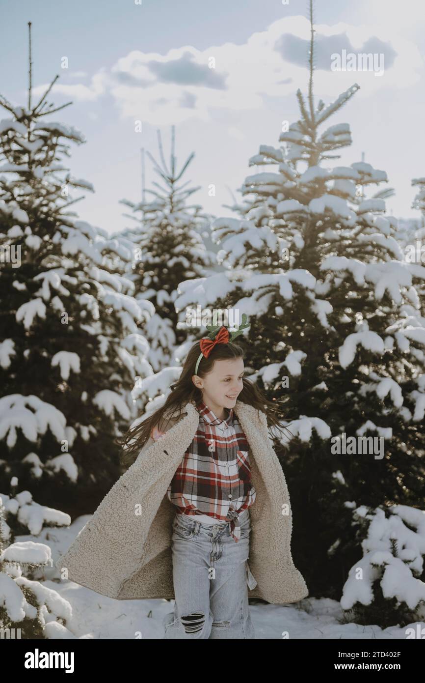 Girl in a winter coat in front of snow-covered fir trees Stock Photo