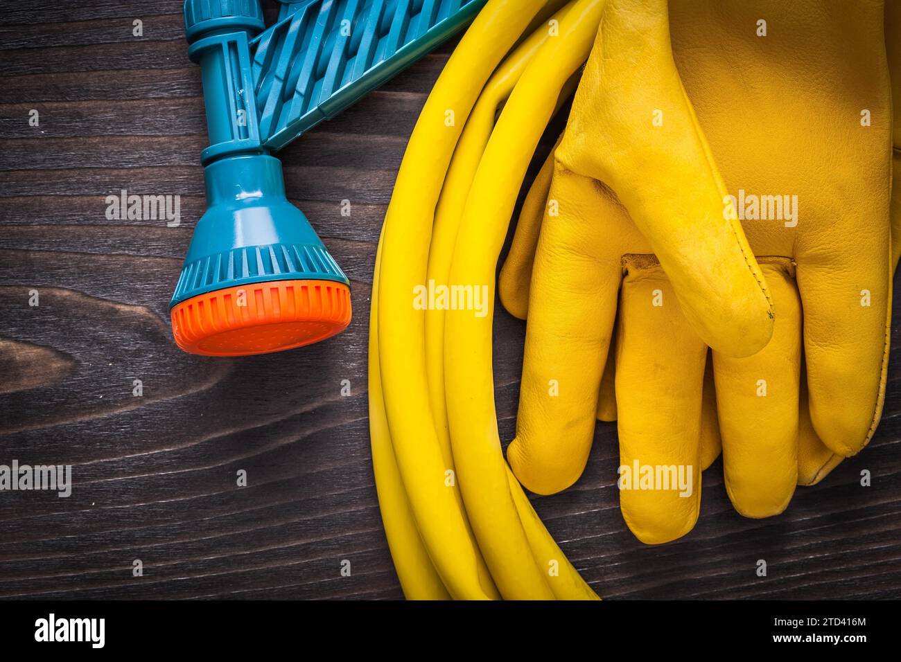 Leather safety gloves and hand spraying hose with water sprinkler on vintage wooden surface farming concept Stock Photo