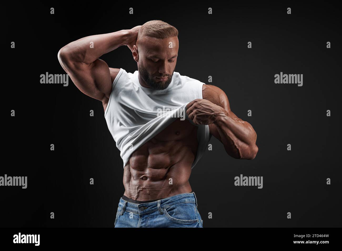 Muscular model man in white t-shirt on a black background. Sporty guy showing his big shoulders, biceps, triceps, abs. Workout, bodybuilding, people Stock Photo