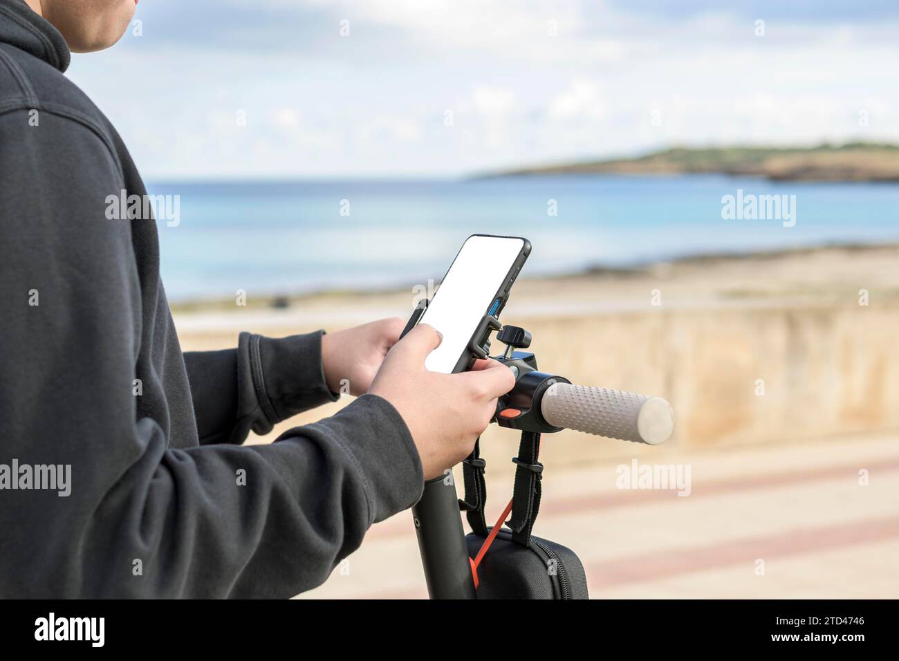 Person holding a smartphone while standing with a scooter by the sea Stock Photo